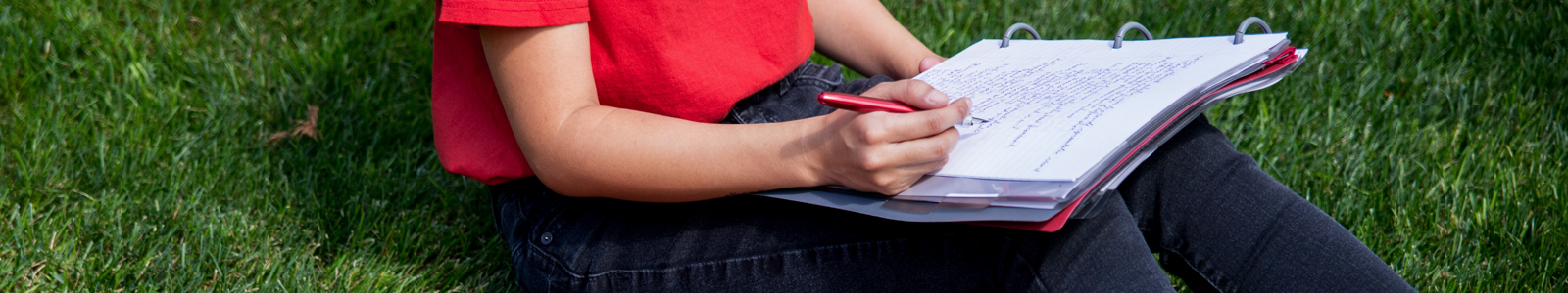 Banner photo featuring a person sitting in the grass and writing in a notebook