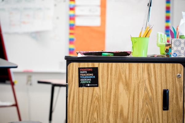 Photo features a wooden desk with a pencil holder filled with pencils, a box of tissues, and a stack of books.
