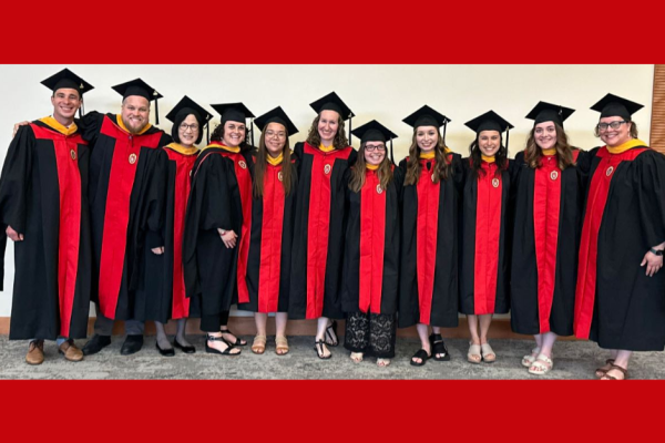 MSPE graduates standing in a line, dressed in graduation regalia, smiling at the camera.
